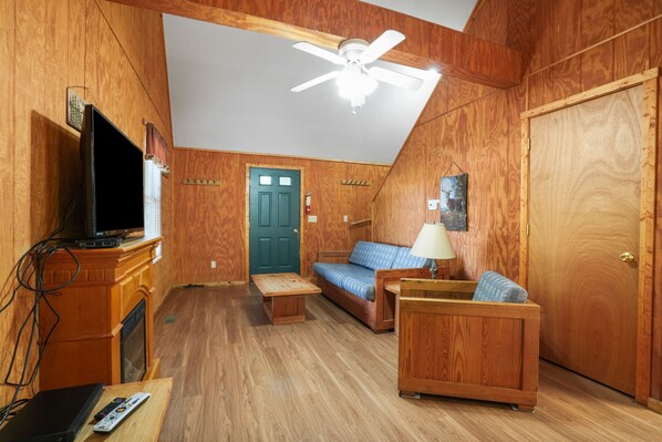 A cozy wooden room with a television, sofa, and a ceiling fan.