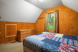 A bedroom with a wooden wardrobe, a bed with a quilt, and a window with curtains.