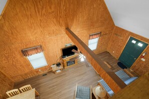 Ein kleiner, hölzerner Raum mit einem Bett, einem Schreibtisch, einem Fernseher und einem Fenster mit Vorhängen.