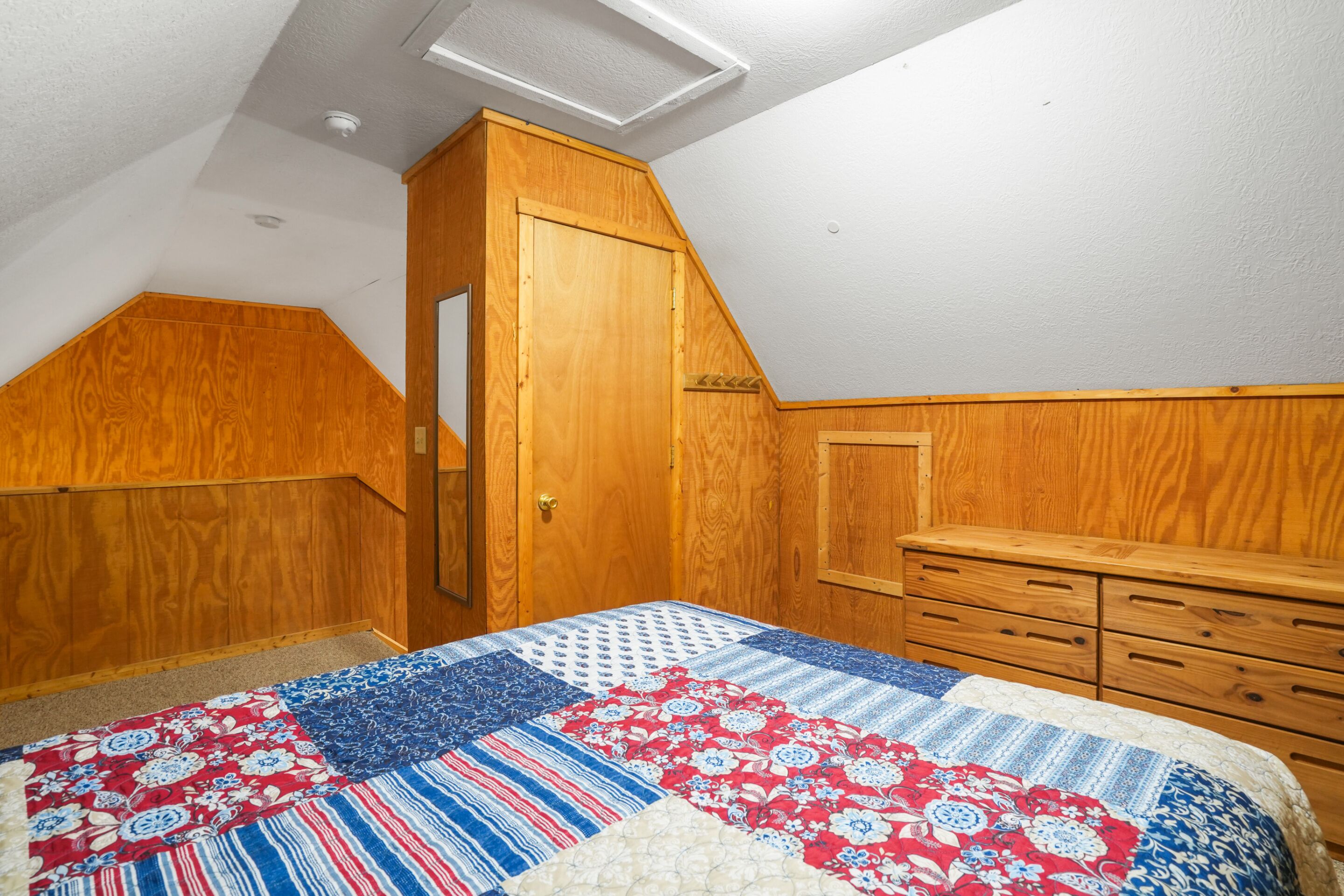 A bedroom with a wooden wardrobe, a bed with a quilt, and a sloped ceiling.