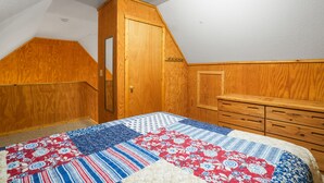 Een slaapkamer met een houten garderobe, een bed met een sprei en een schuine balkenkap.