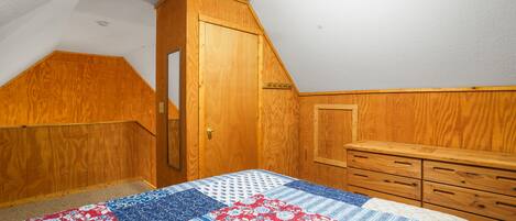 A bedroom with a wooden wardrobe, a bed with a quilt, and a sloped ceiling.