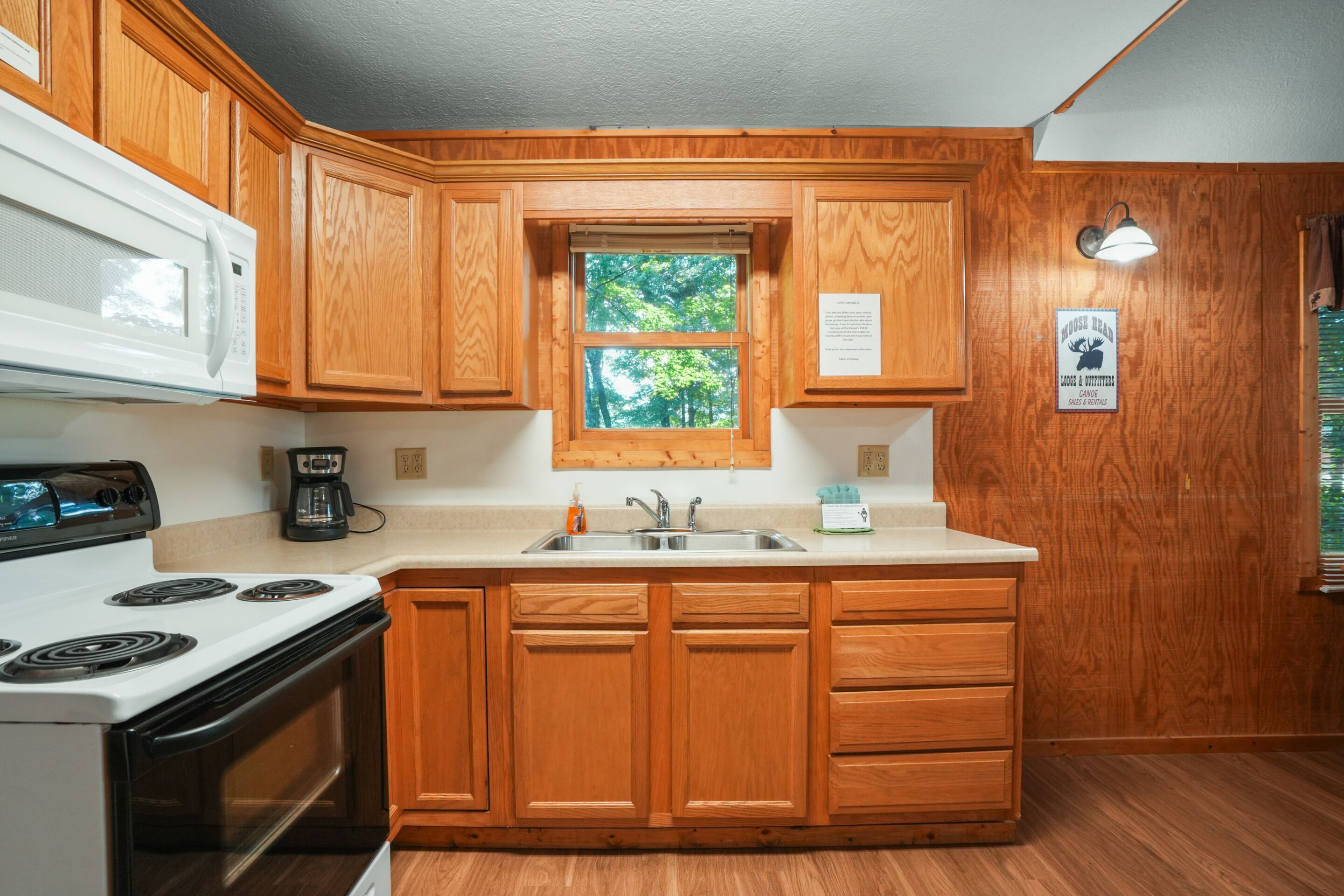 A kitchen with wooden cabinets, a white stove, and a window with a view of trees.