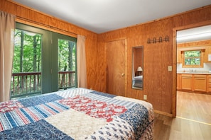 Un dormitorio con una cama grande, paredes de madera, una ventana con cortinas y vistas a árboles.
