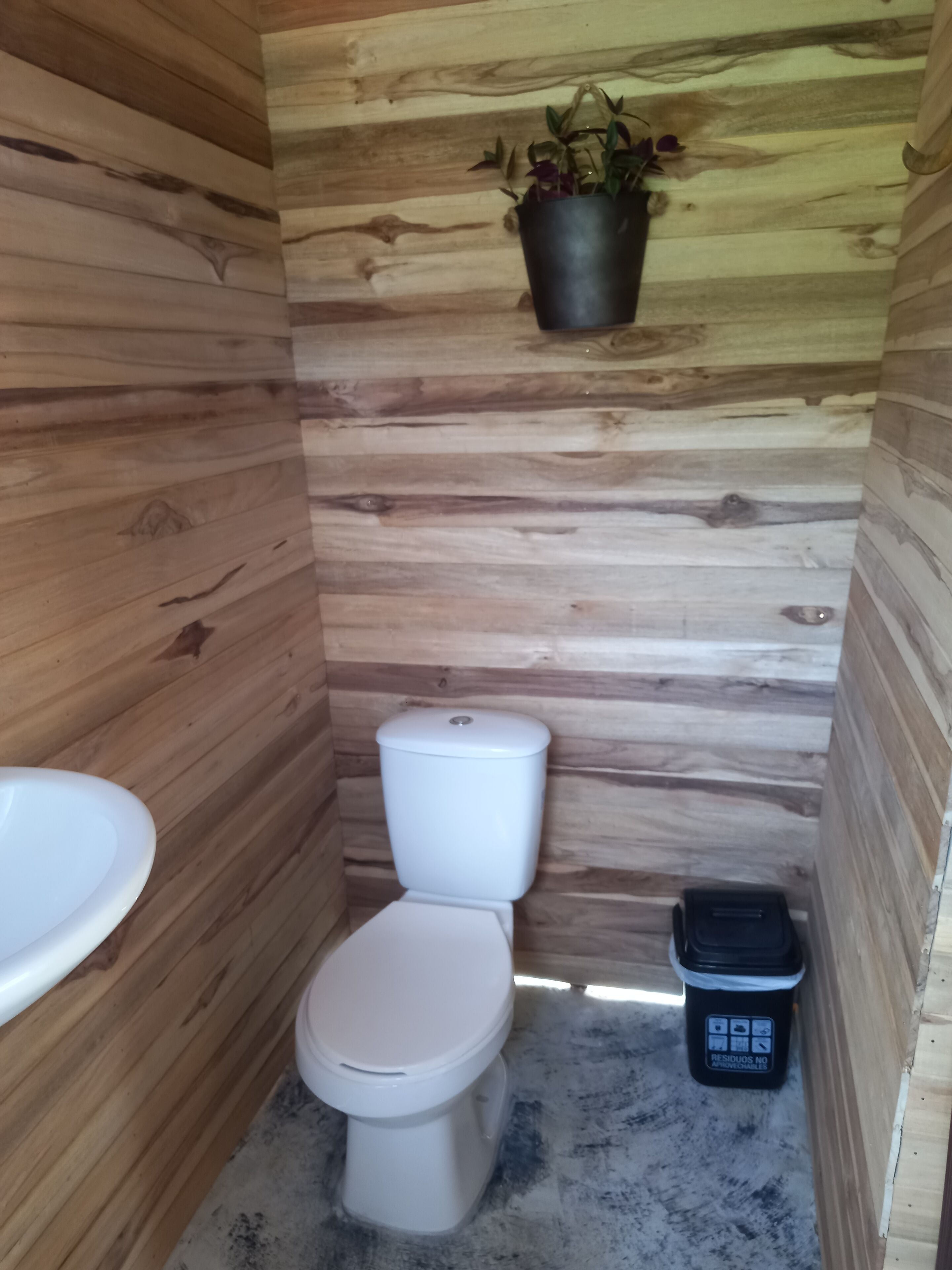 Une petite salle de bain en bois, équipée de toilettes, d’un lavabo et d’une poubelle.