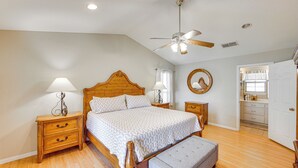 A bedroom with a wooden bed, two bedside tables with lamps, a ceiling fan, and a door leading to a bathroom. - ‘Rhodes Retreat’ w/ Dock on Cedar Creek Lake! (Log Cabin)