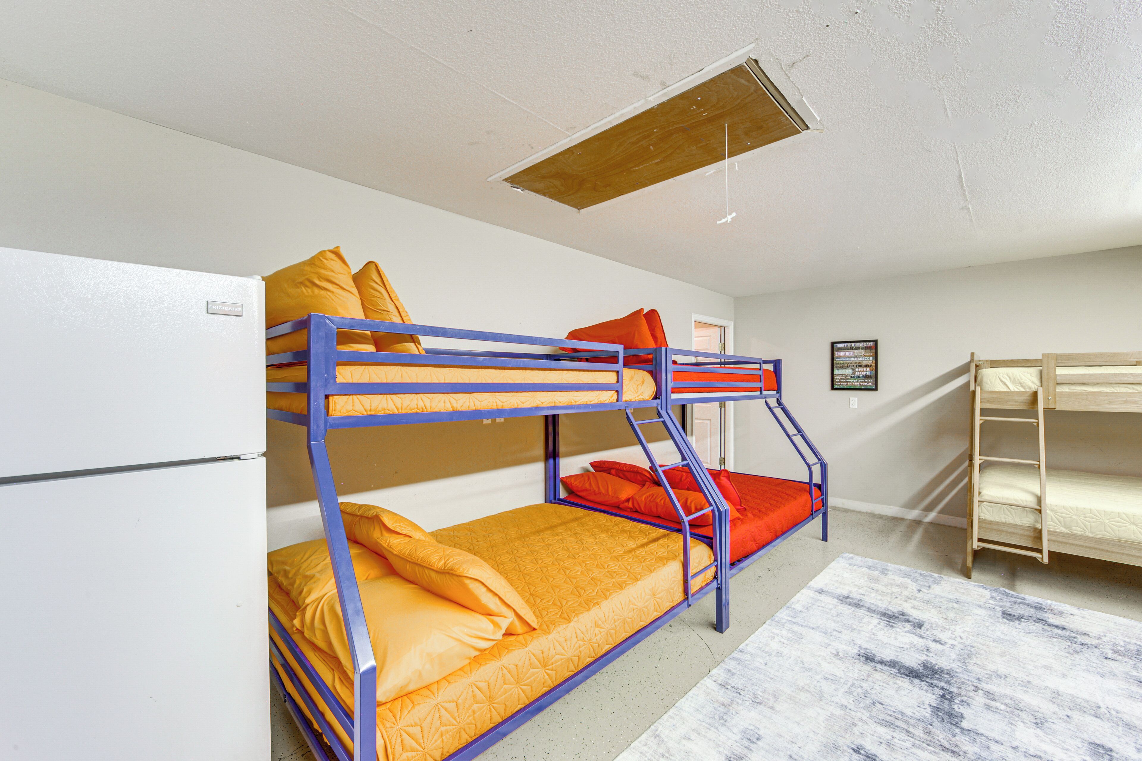 A bunk bed room with a wooden ladder, a white wall, and a framed picture on the wall.