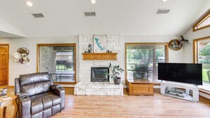 A living room with a stone fireplace, leather sofa, and a flat-screen TV. - ‘Rhodes Retreat’ w/ Dock on Cedar Creek Lake! (Log Cabin)