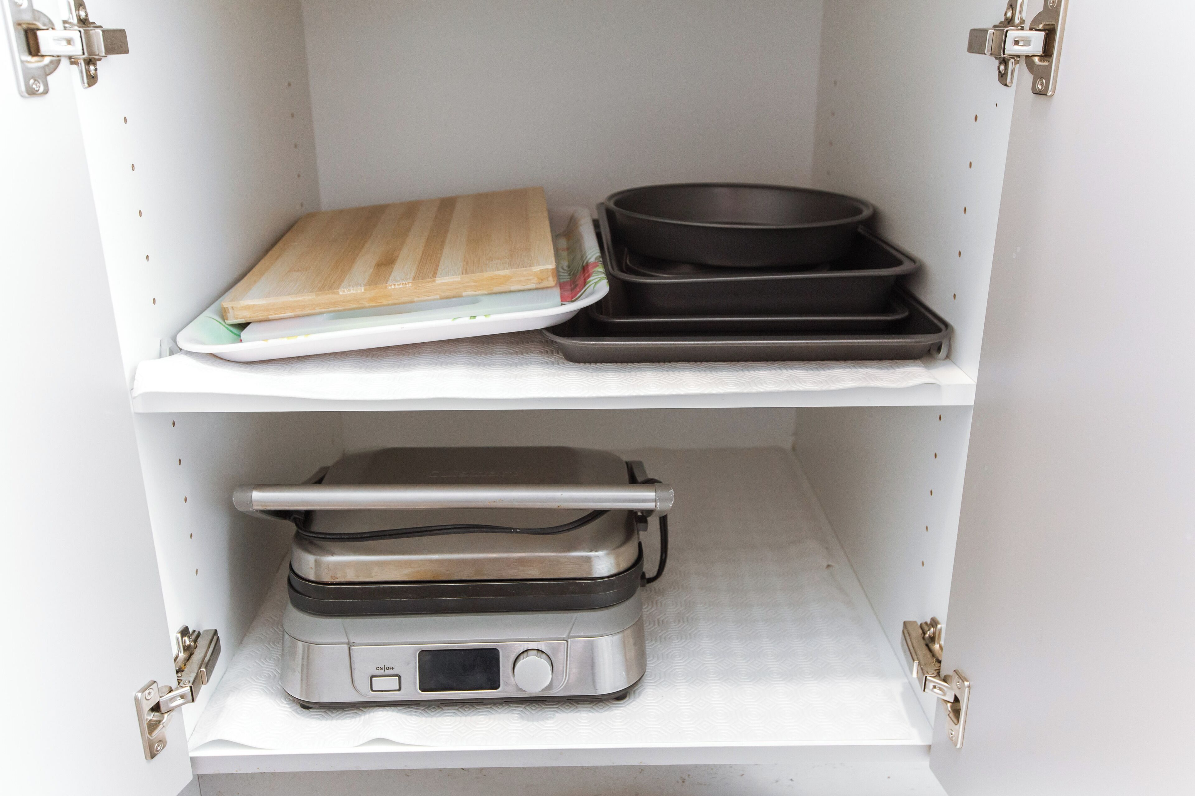 A kitchen with a toaster, a cutting board, and a frying pan on the shelves.