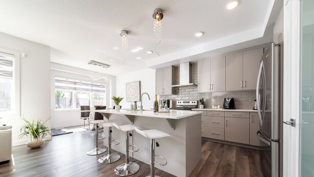 Una cocina moderna con una isla central, taburetes de bar, electrodomésticos de acero inoxidable y un refrigerador grande.