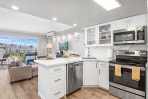 A modern kitchen with white cabinetry, a dishwasher, a microwave, and an oven. - 15th floor Waikiki studio - lanai & pool access (Honolulu)