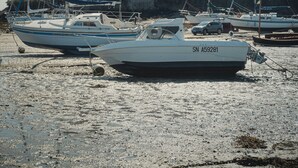 En småbåtshamn med flera båtar förtöjda, en slottsliknande byggnad i bakgrunden och en sandstrand.