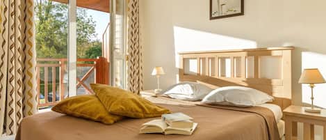 A bedroom with a large bed, two bedside tables, a window with curtains, and a balcony.