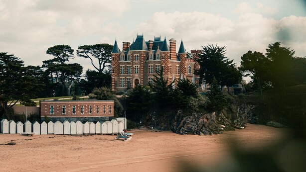 Un edificio grande con aspecto de castillo, con múltiples torres y una playa de arena al frente.