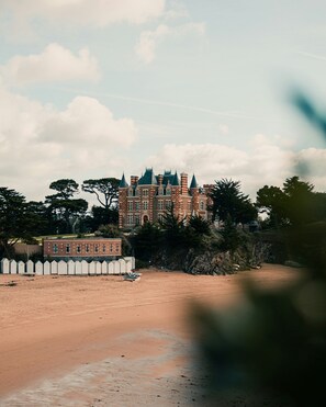 A large, castle-like building with multiple towers and a sandy beach in the foreground. - T3 confortable | En bord du mer + espace bien-être (Saint-Briac-sur-Mer)