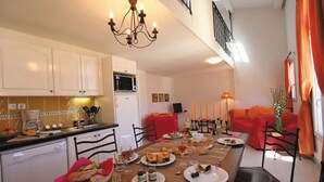 Ein Essbereich mit einem langen Tisch, gedeckt für eine Mahlzeit, einer Küche im Hintergrund und einem roten Sofa im Wohnbereich.