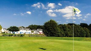 Un terrain de golf avec un drapeau, une rangée de maisons colorées et un ciel dégagé.
