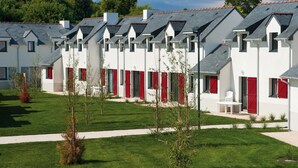 Une rangée de bâtiments modernes, blancs, avec des volets rouges et des toits inclinés, entourés de pelouses bien entretenues et de petits arbres.