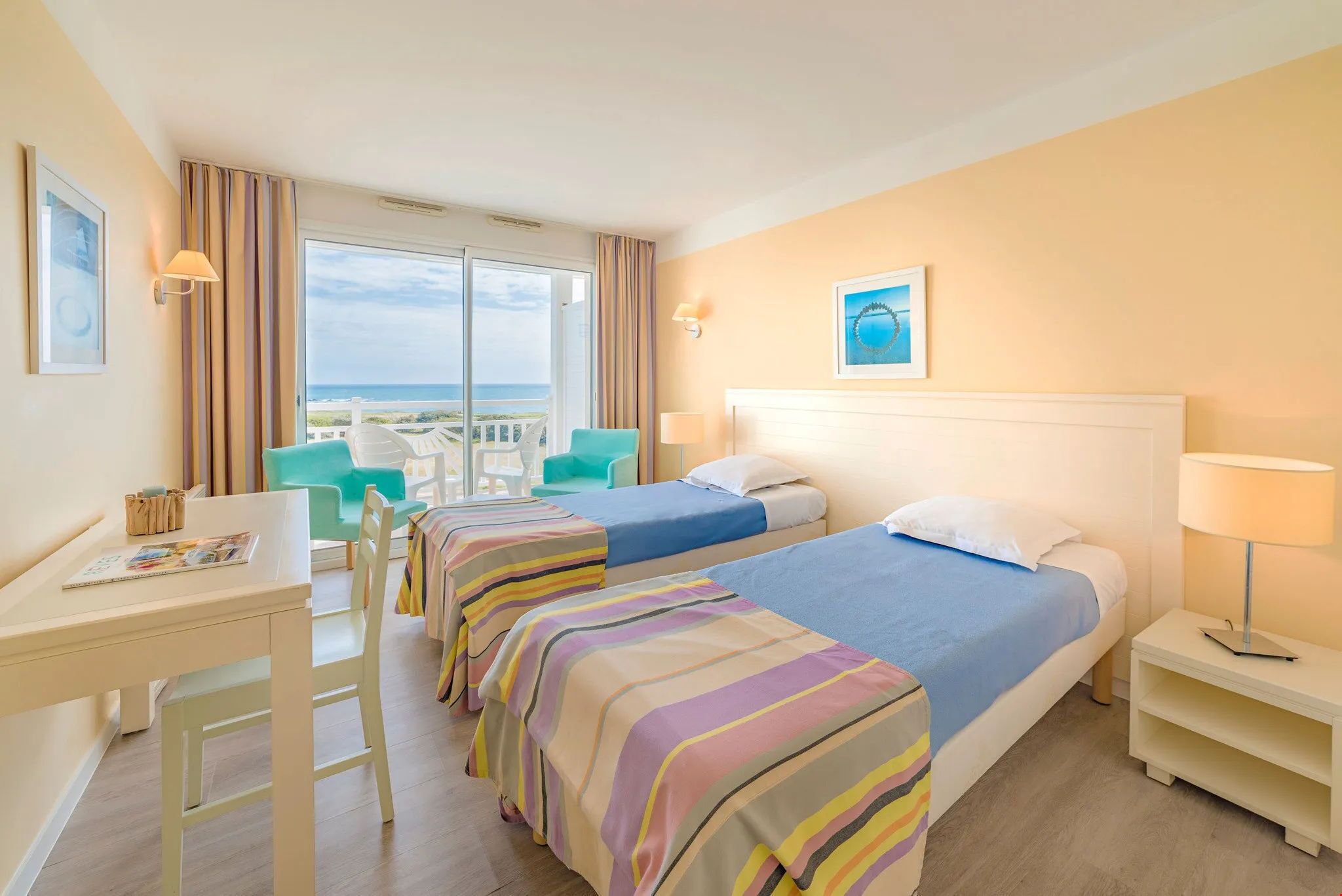 Ett hotellrum med två sängar, ett skrivbord och utsikt över havet.