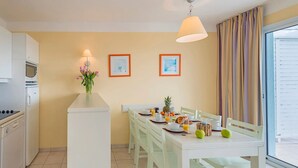 A kitchen with white cabinets, a dining table set with plates, cups, and a vase of flowers. - T3 proche de la mer + 2 piscines sur place ! (Château-d'Olonne)