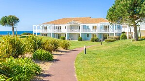 A coastal hotel with a paved pathway leading to the entrance, surrounded by well-maintained lawns and pine trees. - T3 proche de la mer + 2 piscines sur place ! (Château-d'Olonne)