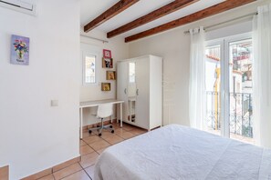 A bedroom with a bed, a desk, a chair, a wardrobe, and a balcony with a railing.