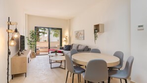 Un soggiorno moderno con un tavolo da pranzo rotondo, sedie grigie, un divano, una TV e una pianta.