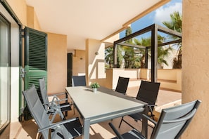 Une terrasse extérieure avec une table et des chaises, un pot de fleurs et une vue sur des palmiers.
