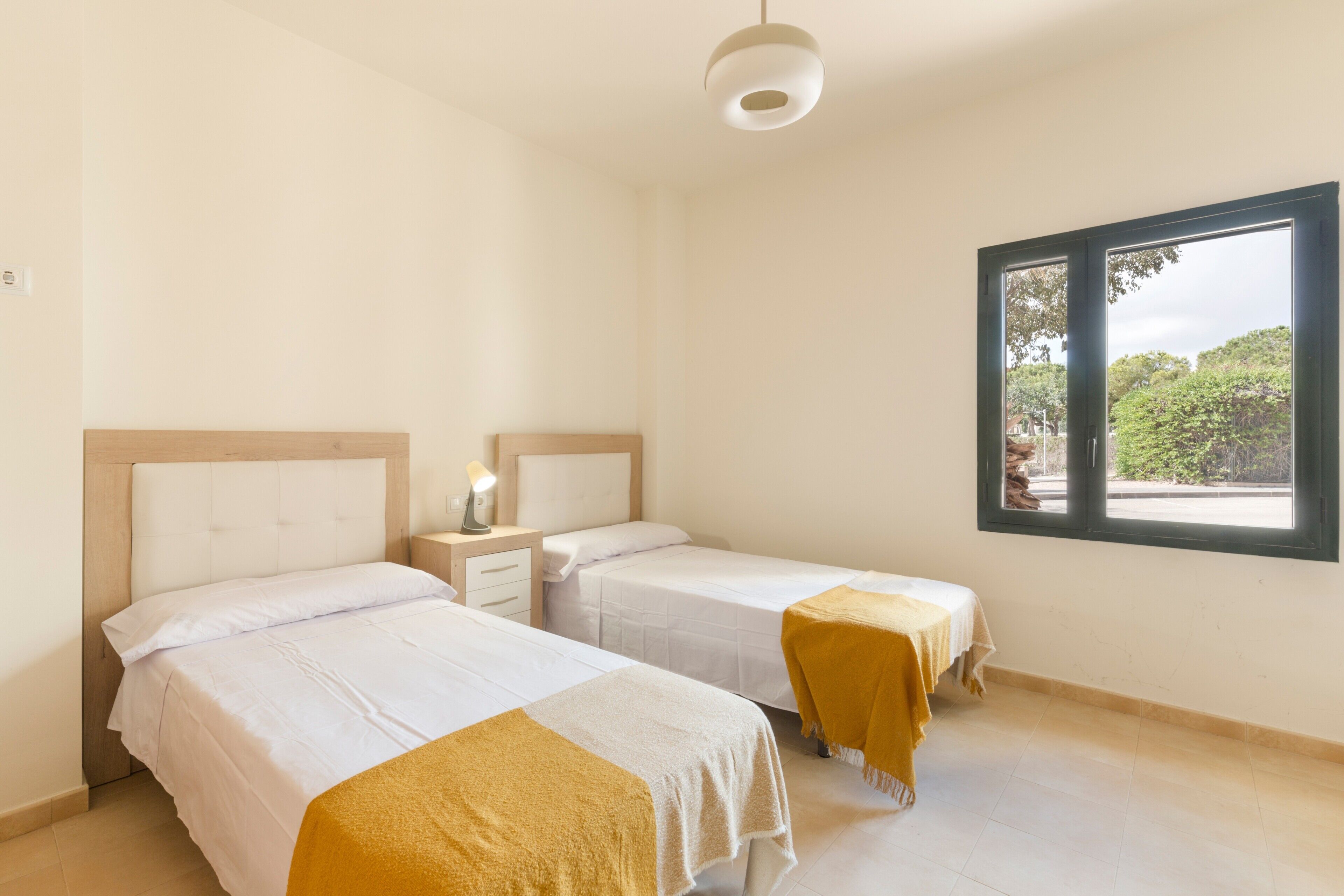 Una habitación con dos camas, una ventana y una mesita de noche con lámpara.