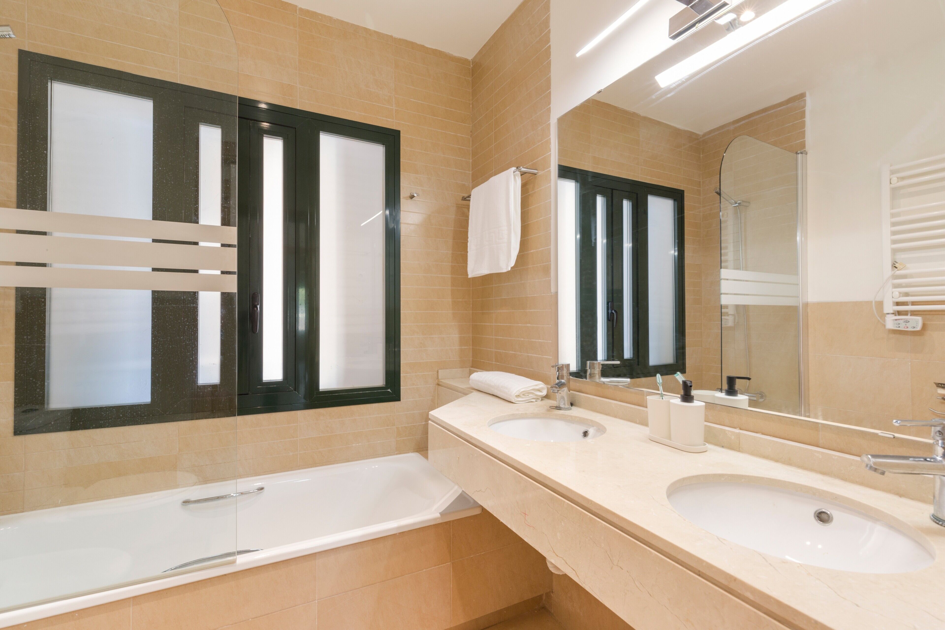 Un baño moderno con dos lavamanos, una bañera y un espejo grande.