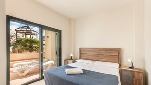 Una camera da letto con un letto, un comodino, una lampada, una finestra vista piscina e palme, e un'ampia porta scorrevole in vetro.