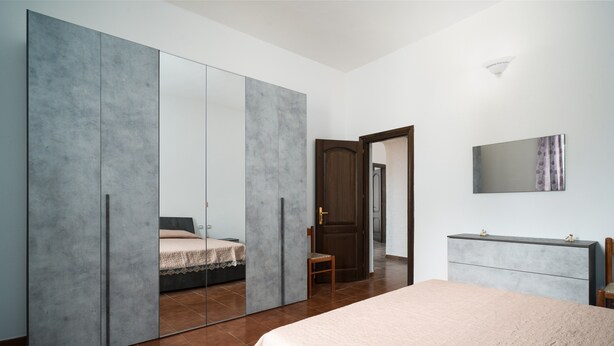 Een slaapkamer met een bed, een garderobe, een dressoir en een spiegel.