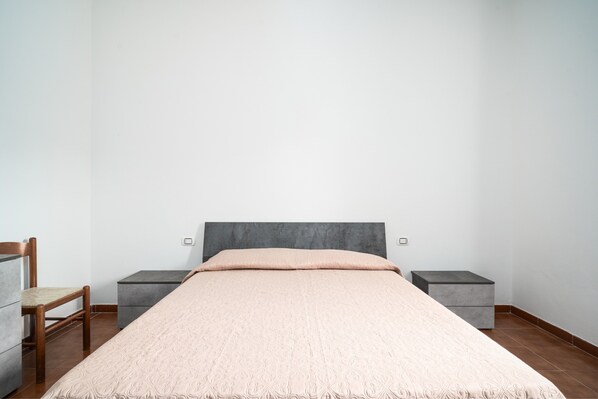 A bedroom with a bed, two bedside tables, a chair, and a wardrobe.