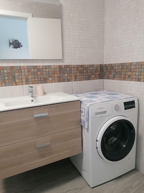 Ein modernes Badezimmer mit einem weißen Waschbecken, einem Spiegel, einer Toilette und einer Waschmaschine.