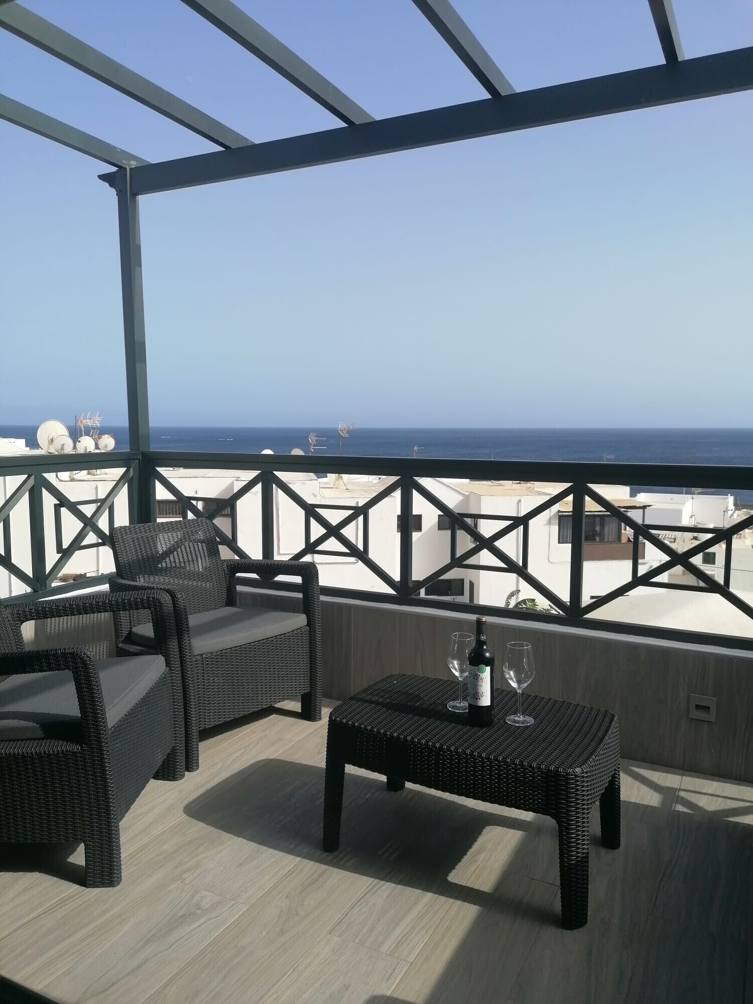 Ein Balkon mit Korbmöbeln, einem Tisch mit Flasche und Glas sowie Meerblick.