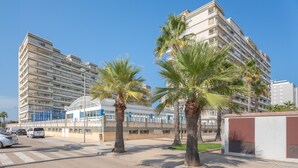 Een meerhoog gebouw met balkons, palmbomen en een helderblauwe lucht.