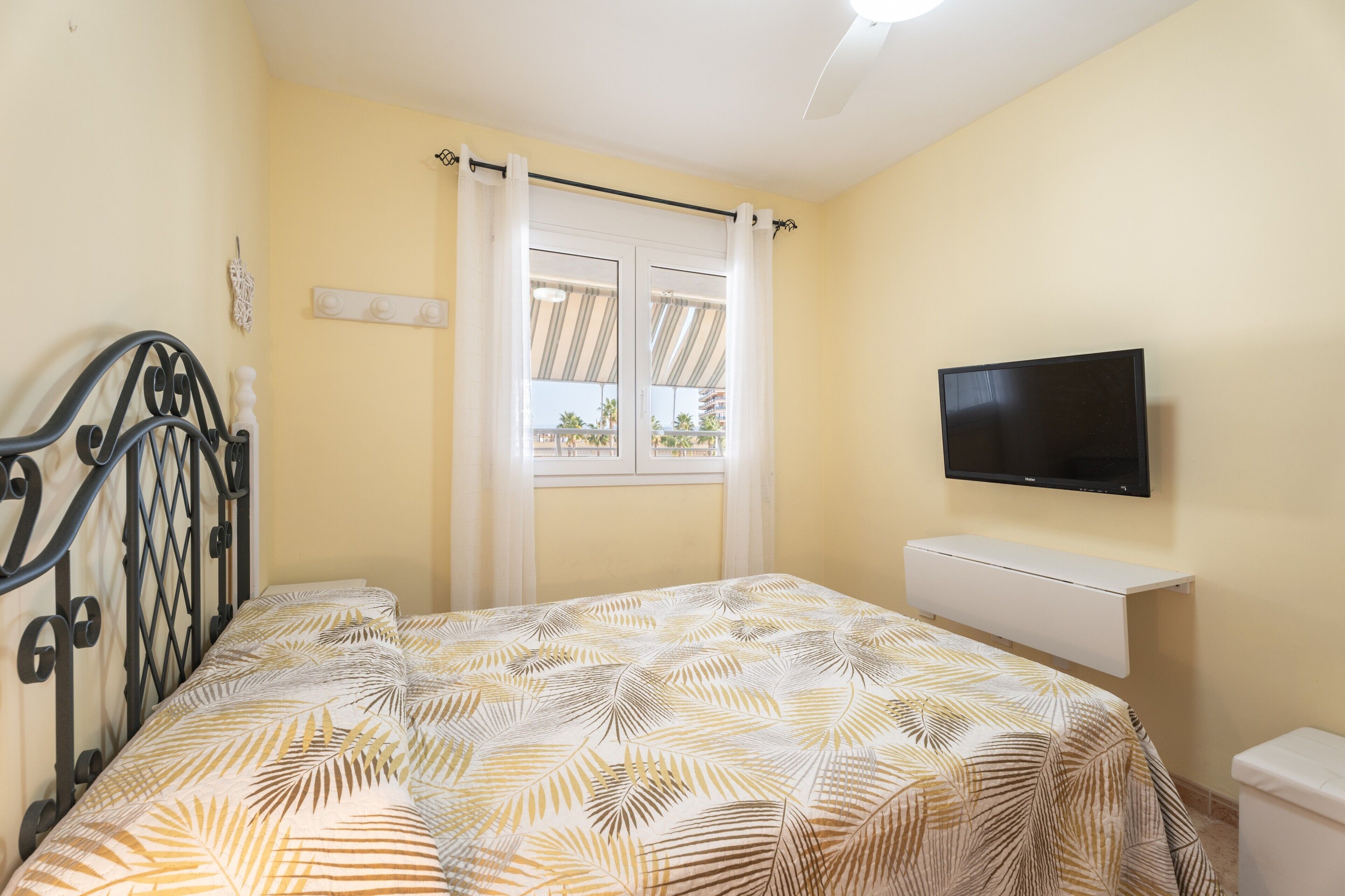 A bedroom with a bed, a TV, a window with curtains, and a ceiling fan.