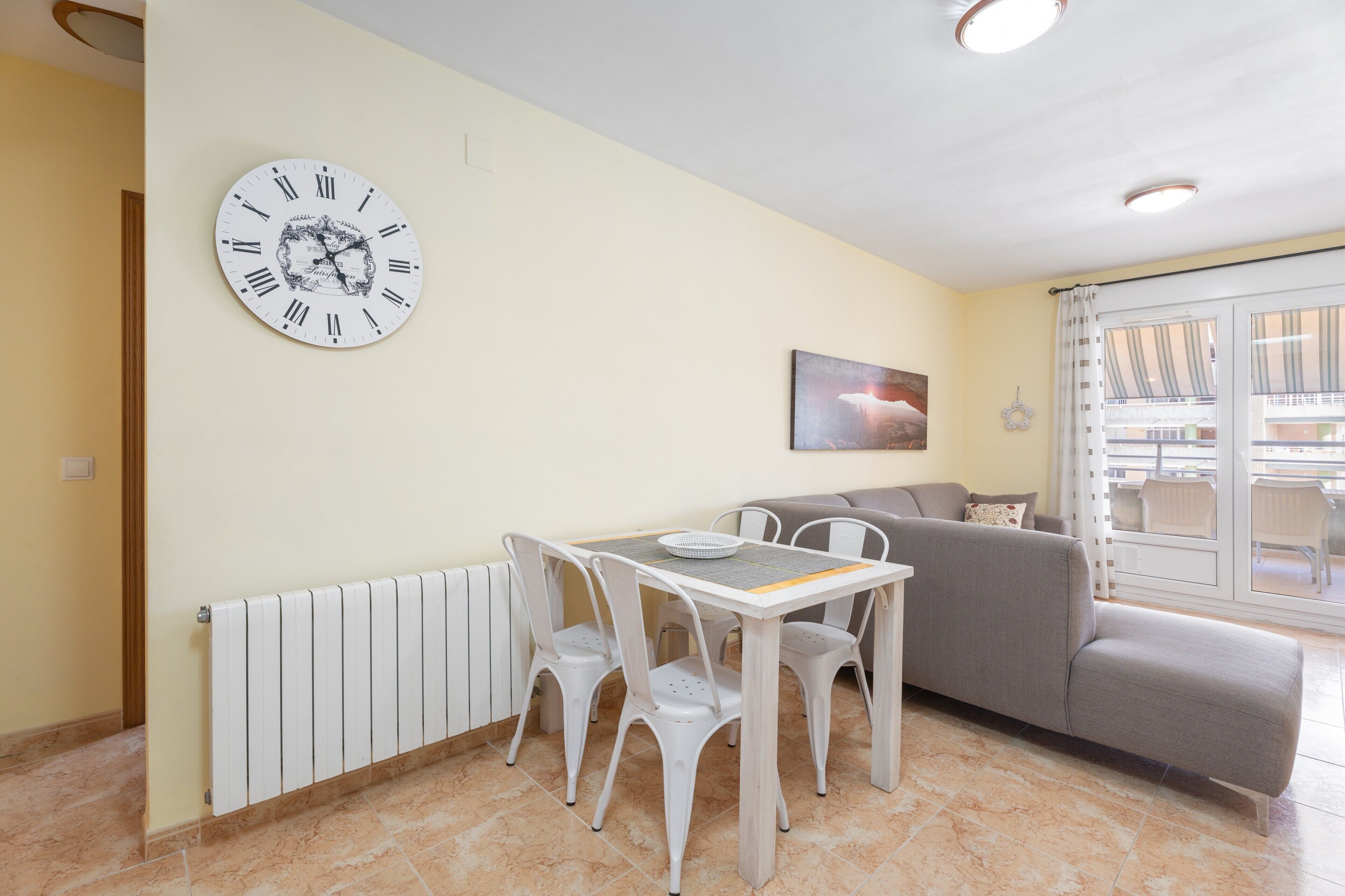 Una sala de estar con una mesa de comedor, sillas, un sofá, un reloj de pared y un ventanal con vistas.