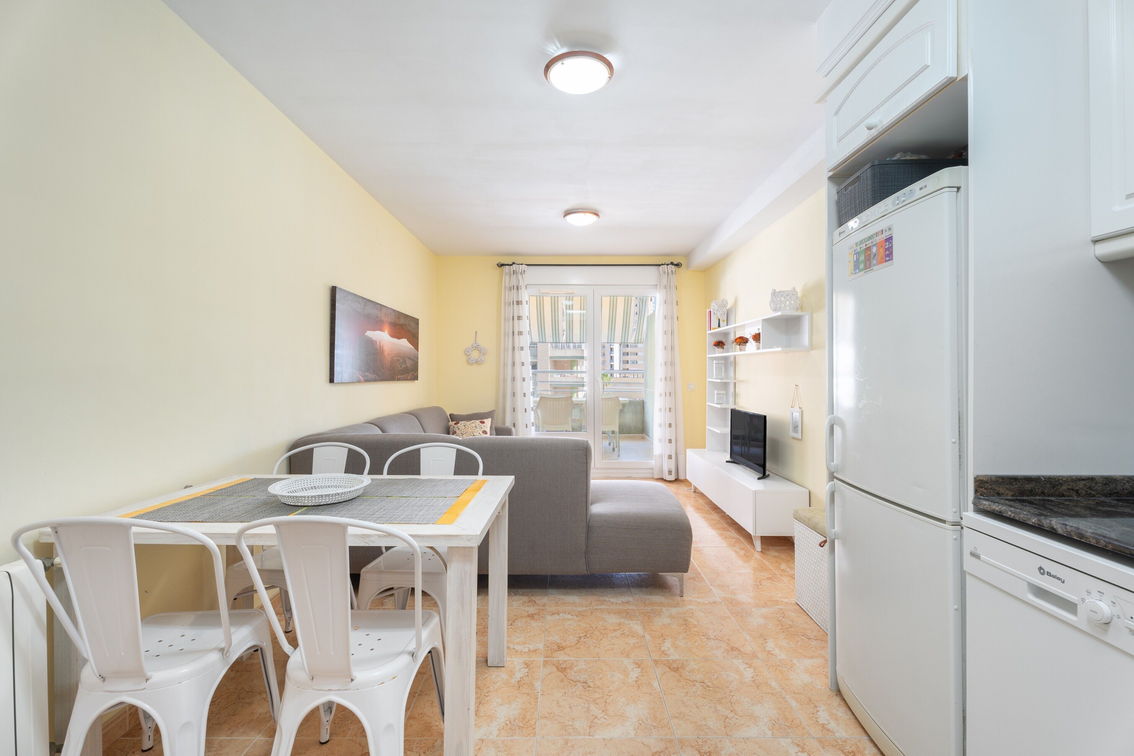 Een ruimtelijk ingerichte leefruimte met een eethoek, een bank en een kitchenette.