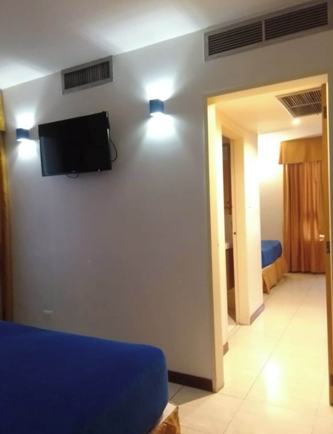 Une chambre d’hôtel avec un lit, un téléviseur fixé au mur et une salle de bain visible à travers une porte ouverte.