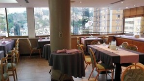 A restaurant with multiple tables and chairs, large windows with a city view, and a tiled floor. - Hotel las Americas (Caracas)