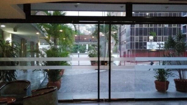 A hotel lobby with a glass door entrance, potted plants, and a doormat. - Hotel las Americas (Caracas)