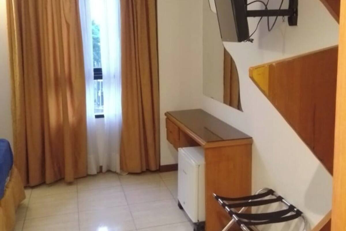 A compact room with a desk, a chair, a TV mounted on the wall, and a window with curtains.