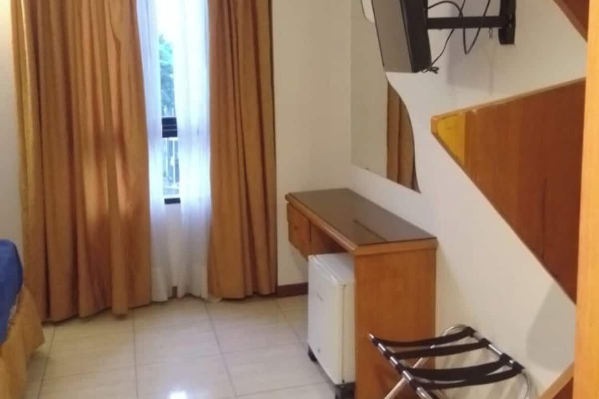A compact room with a desk, a chair, a TV mounted on the wall, and a window with curtains.