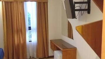 A compact room with a desk, a chair, a TV mounted on the wall, and a window with curtains.