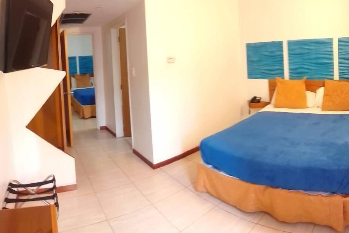 A hotel room with a large bed, a TV, and a view of the sea through the window.