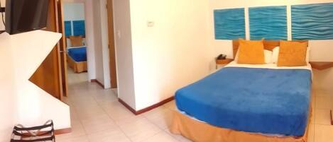 A hotel room with a large bed, a TV, and a view of the sea through the window.