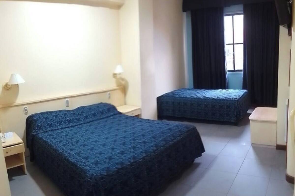 A hotel room with two beds, a desk, and a window with curtains.