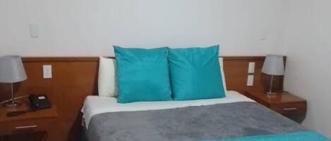 Un dormitorio ordenado con una cama, dos mesitas de noche y un adorno en la pared.