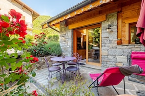 Un bâtiment en pierre avec une façade en bois, une terrasse avec une table et des chaises, et une chaise rouge à l’extérieur.